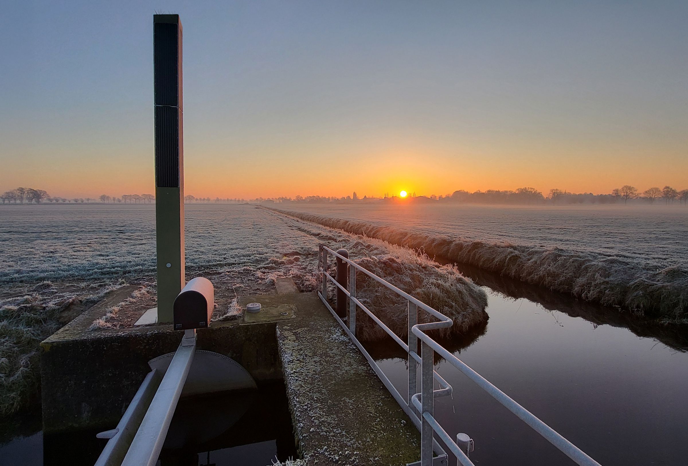 Zonsopkomst boven een stuw in een berijpt polderlandschap